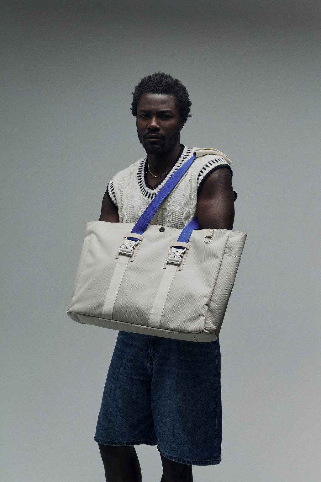 Person holding a large beige bag with blue straps.