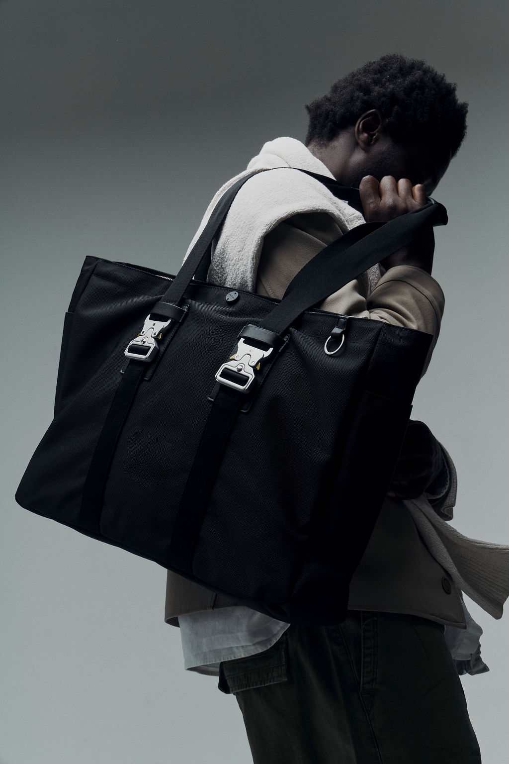 Person holding a large black tote bag with metal buckles.