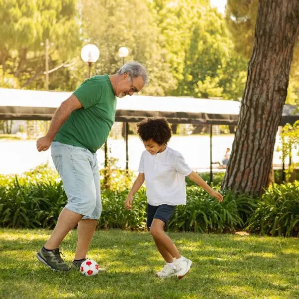 An older man and a young boy play soccer together on a grassy lawn in a park.