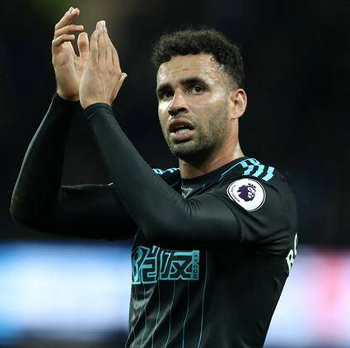 A football player in a black long-sleeved jersey with a Premier League patch claps his hands.