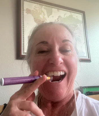 Person smiling and holding a purple toothbrush near their mouth.