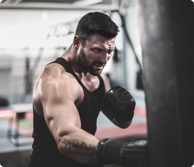 Man in a black tank top punching a boxing bag.