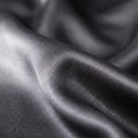 A neatly made bed with grey sateen bedding and pillows, illuminated by sunlight from a window.