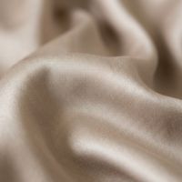 A sunlit bed with champagne-colored satin bedding and white pillows against a textured headboard.