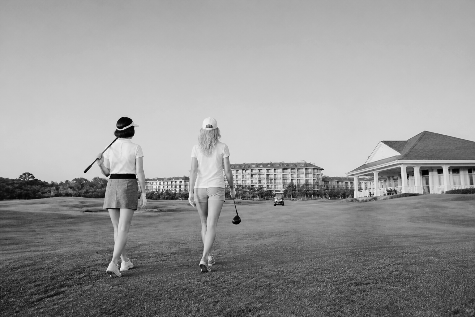 A black and white photograph of two women walking from behind on a golf course, carrying clubs.