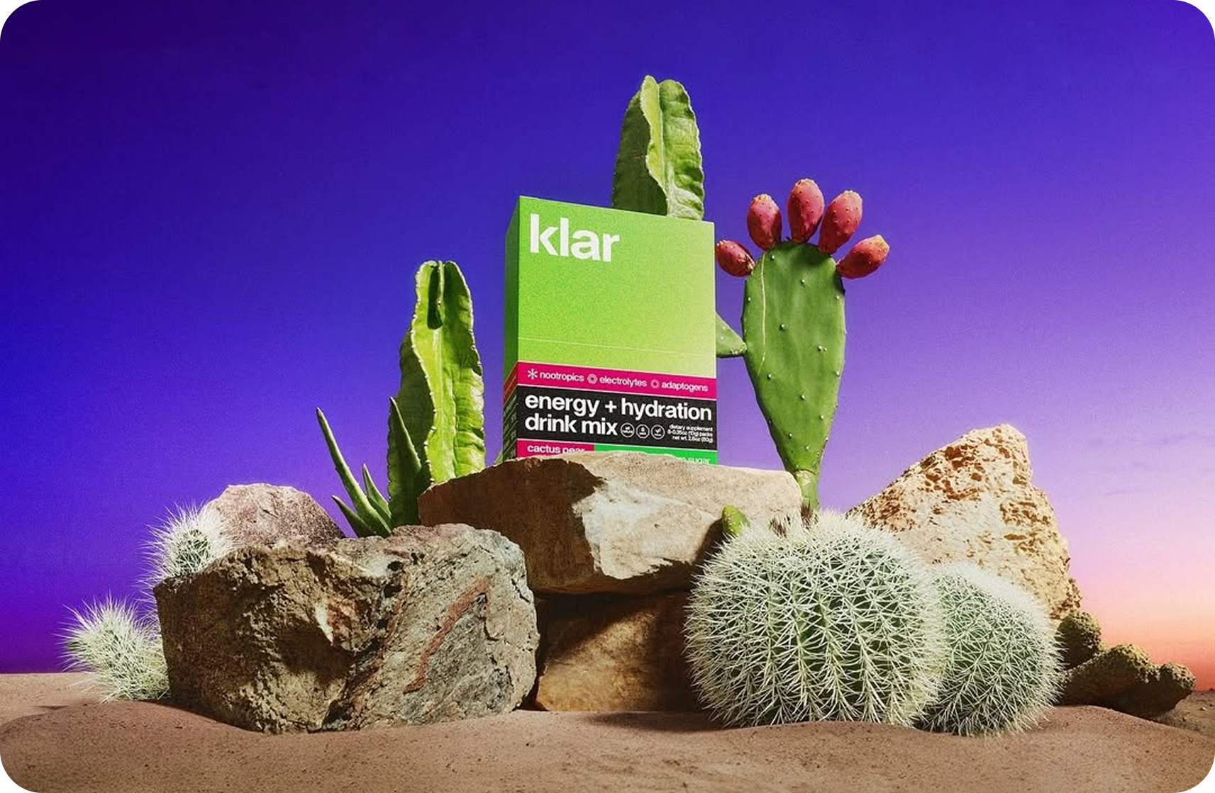 Green energy drink box among cacti and rocks against a purple sky.