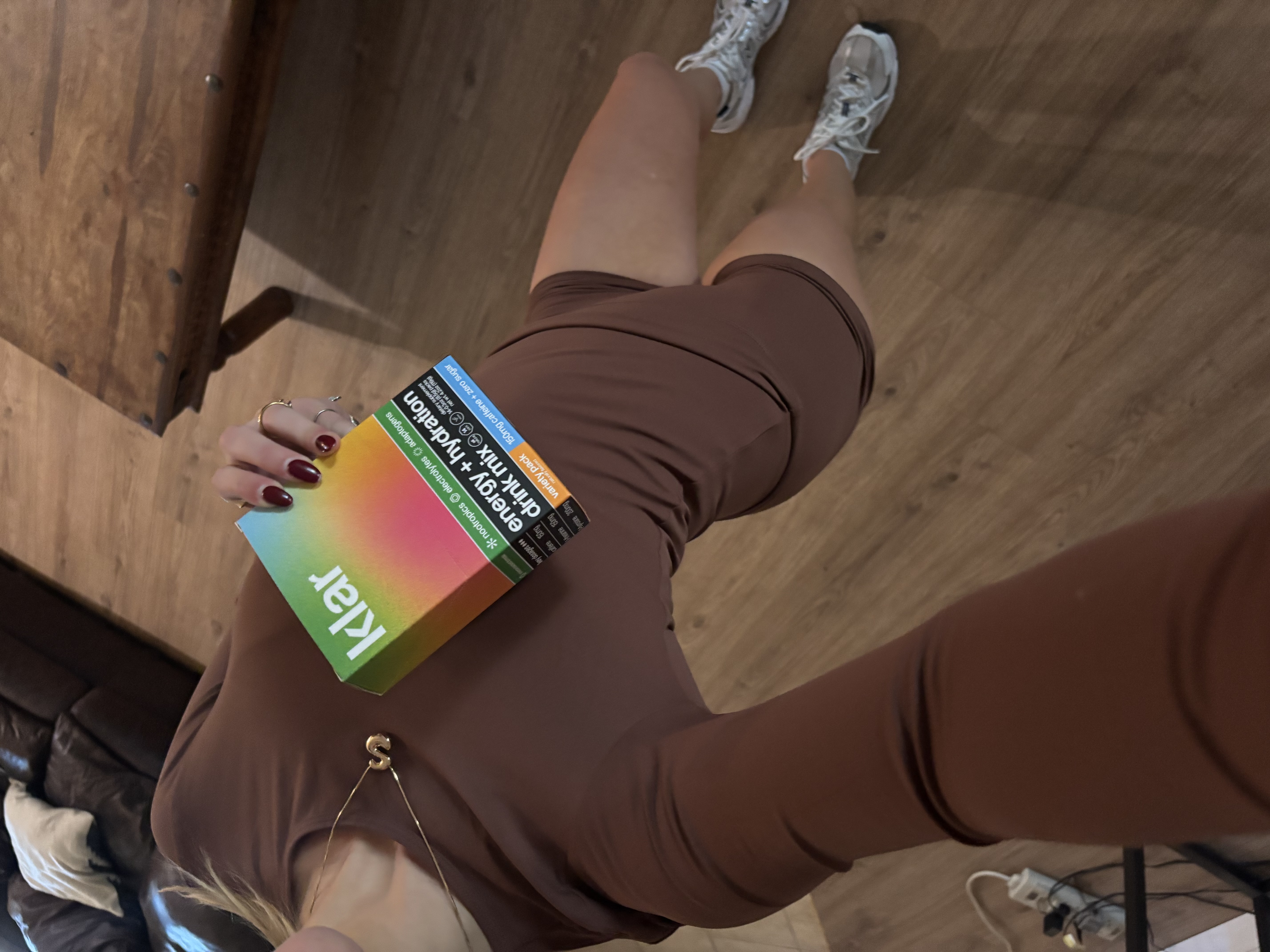 A person in a brown outfit holds a colorful box of Klar energy and hydration drink mix.