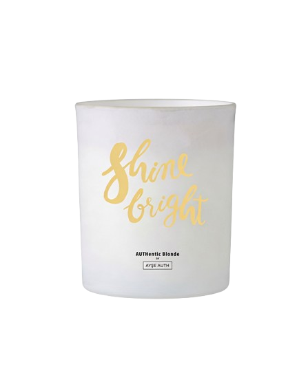 A white candle in a glass jar with 'Shine bright' written in gold script.