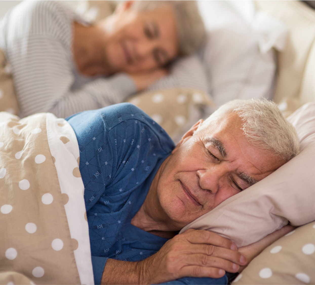 Two elderly people sleeping peacefully in bed with polka dot sheets.