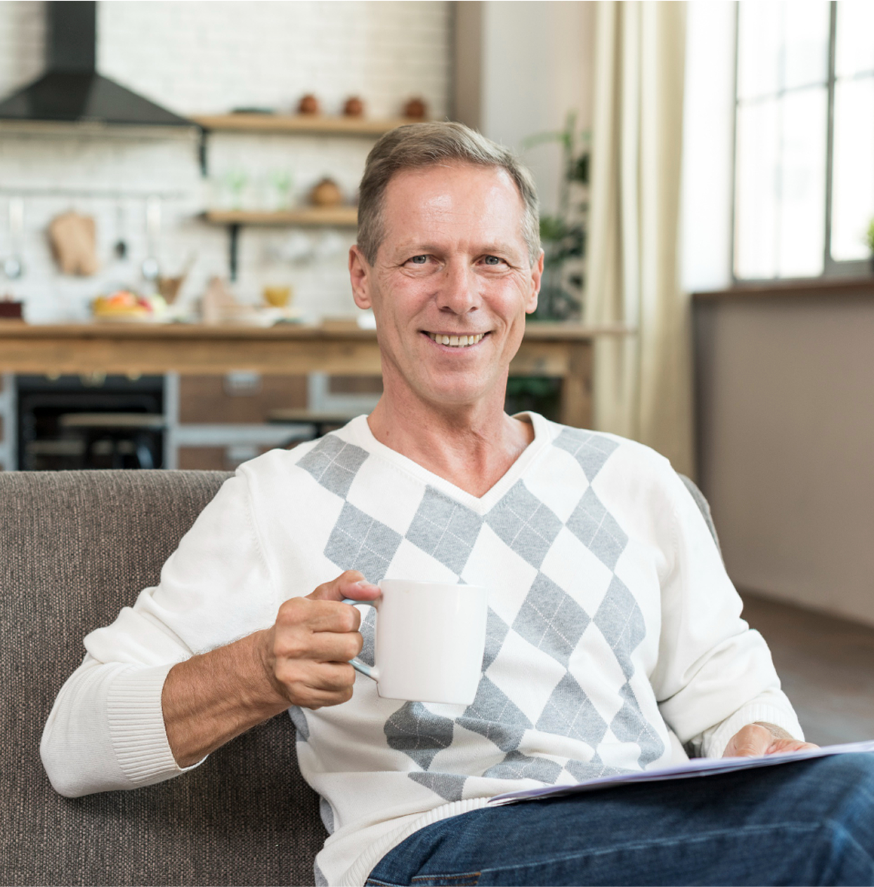 Man sitting on a couch holding a white mug, smiling.