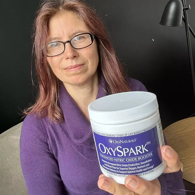 Person holding a container labeled 'OxySpark' beside a black lamp.
