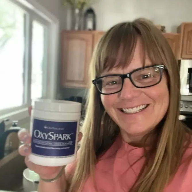 Person holding a container labeled 'OxySpark' in a kitchen setting.
