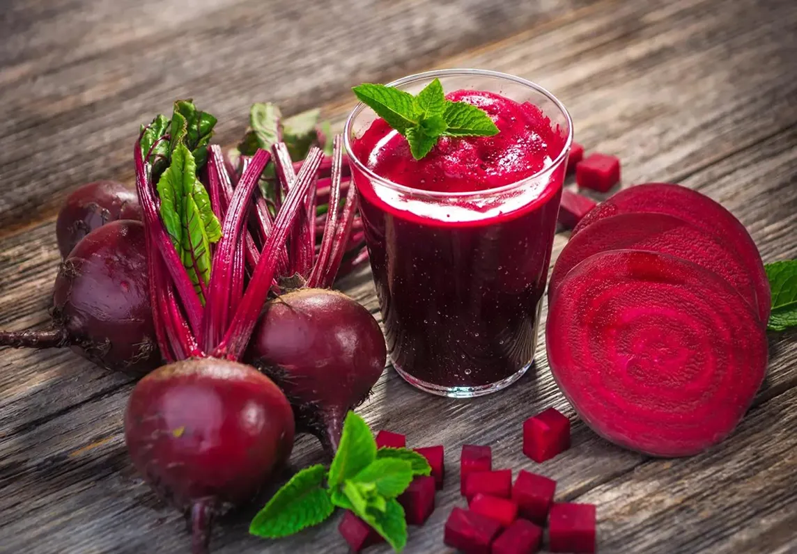 Fresh beets and juice with mint on wooden surface.