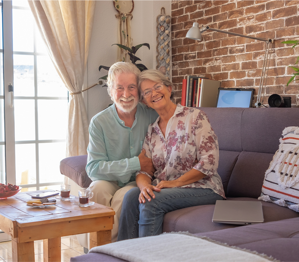 Elderly couple sitting on a couch, smiling in a cozy living room.