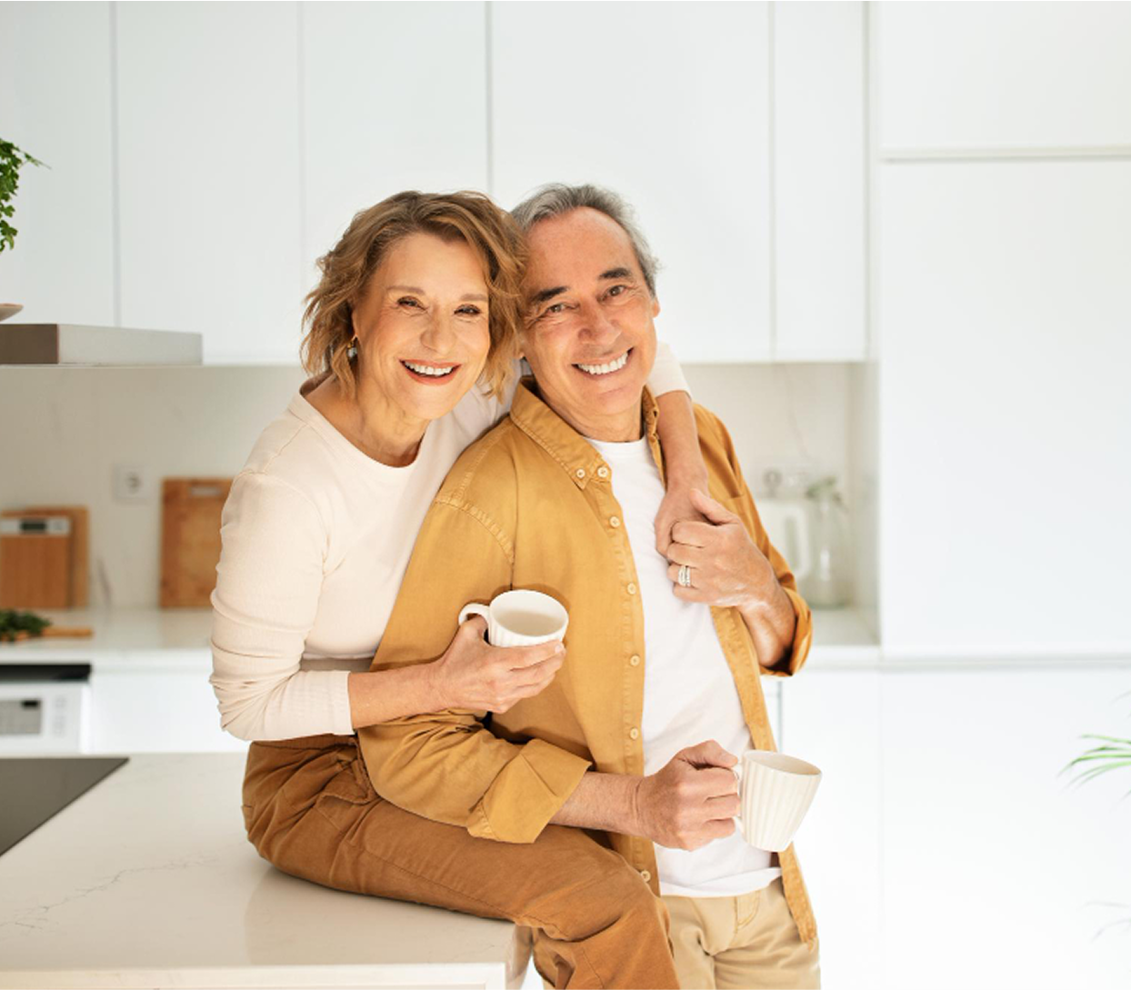 Smiling couple holding mugs in a bright kitchen.