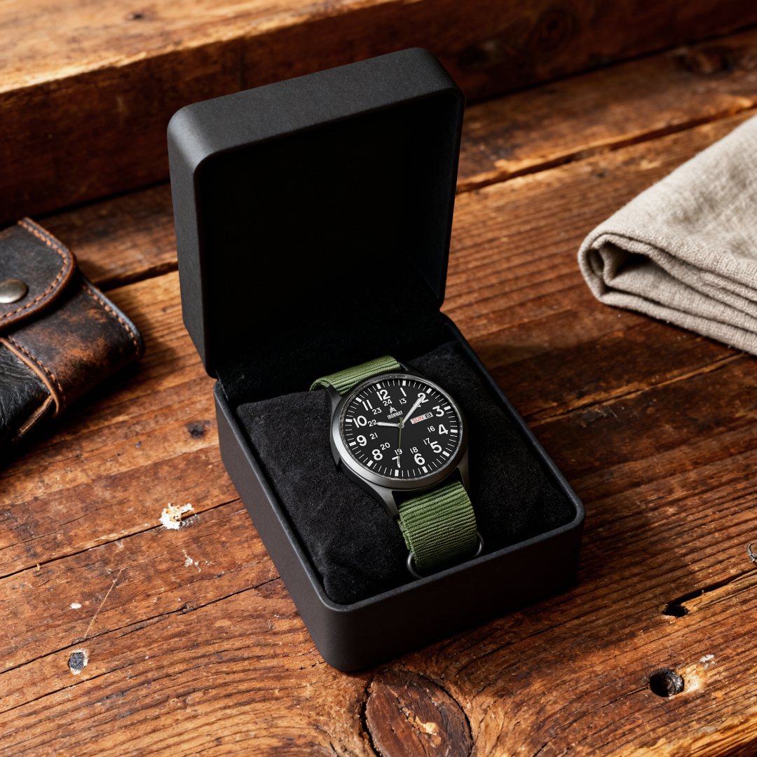 Analog watch with a green strap in an open black box on a wooden surface.