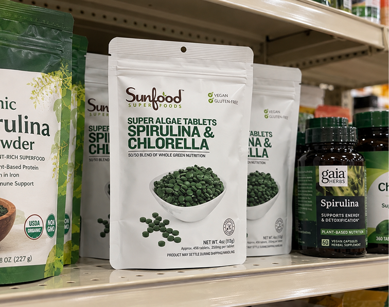 Various spirulina and chlorella supplements in bags and bottles are displayed on a store shelf.