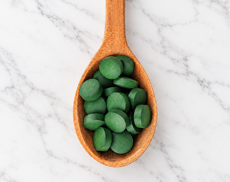 An overhead shot of a wooden spoon full of green tablets on a marble surface.