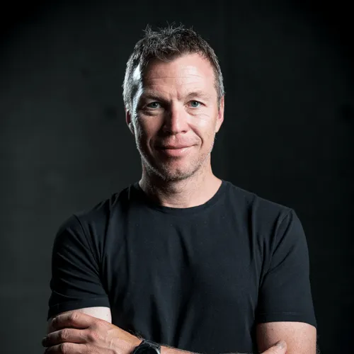 A headshot of a smiling man in a black t-shirt with his arms crossed.