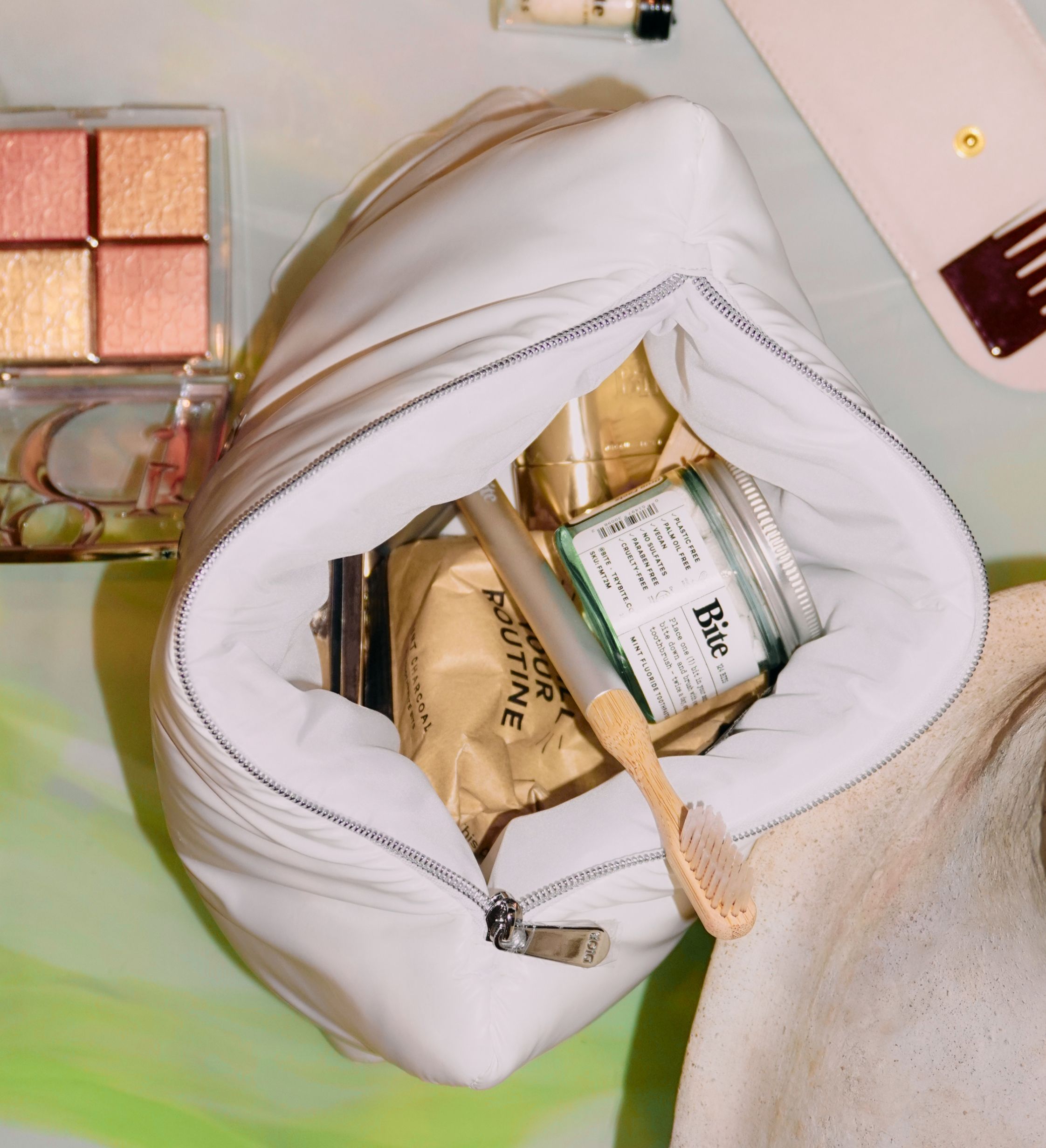 An open white toiletry bag filled with dental products, makeup, and other items on a colorful surface.