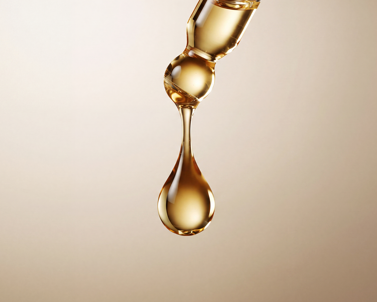 A close-up of a single drop of golden liquid falling from a glass dropper against a beige background.