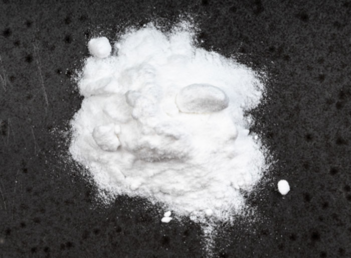 A close-up, overhead shot of a pile of white powder on a dark textured surface.
