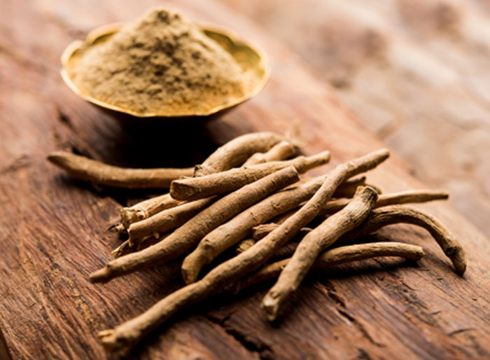 A pile of dried roots and a bowl of light brown powder sit on a wooden surface.
