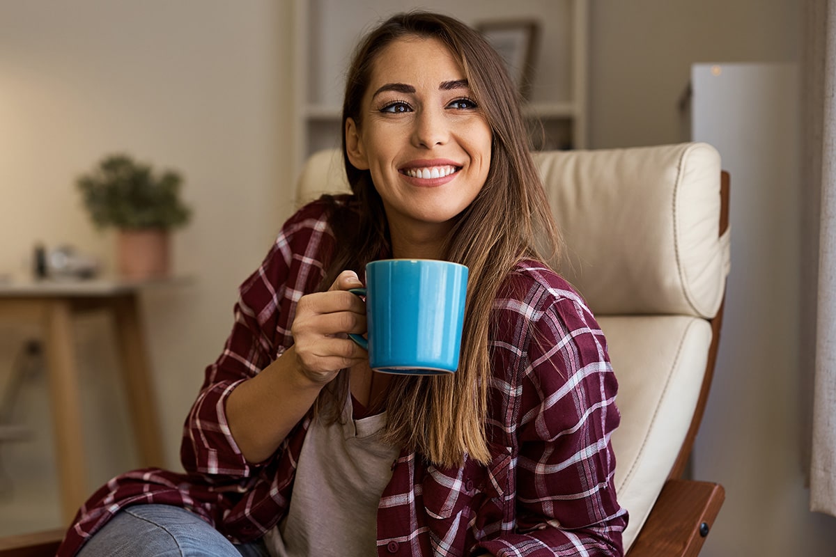 Smiling person holding a blue mug, sitting on a chair indoors.