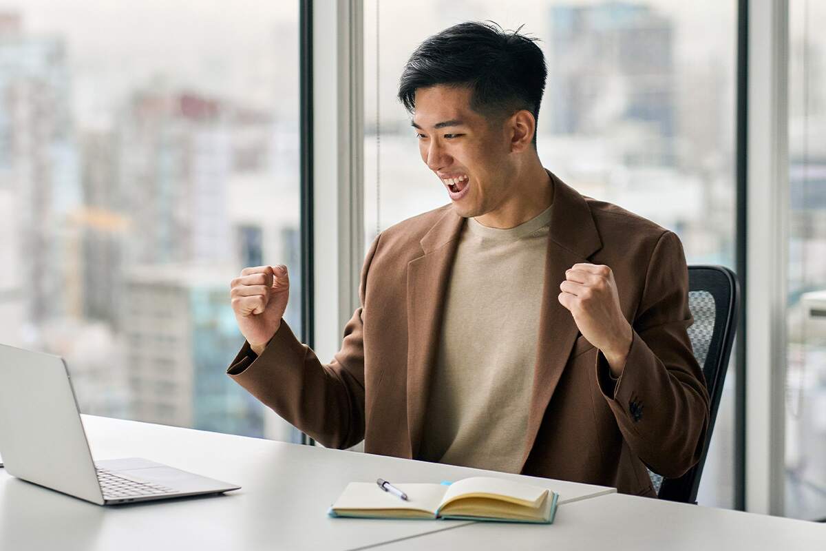 Person celebrating in front of a laptop with fists raised.