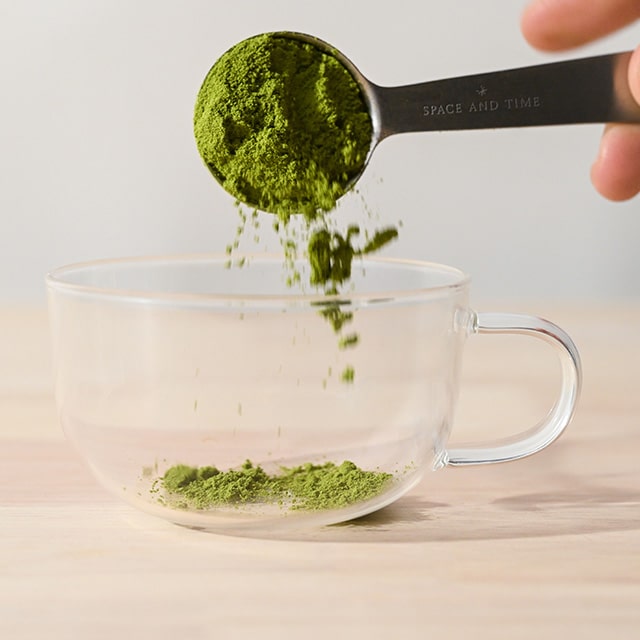 Spoon pouring green powder into a clear glass cup.