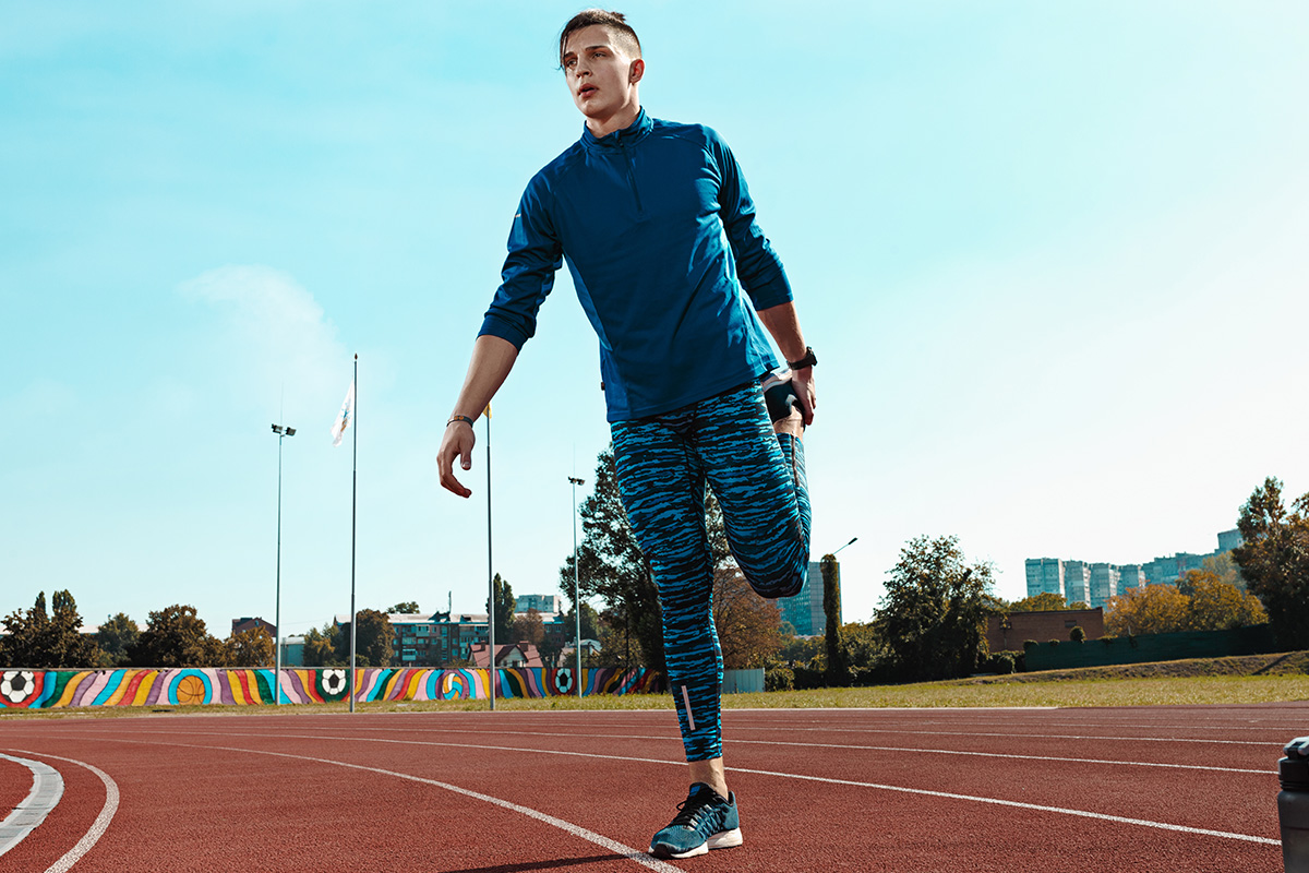 Person stretching on a track field with colorful mural in background.