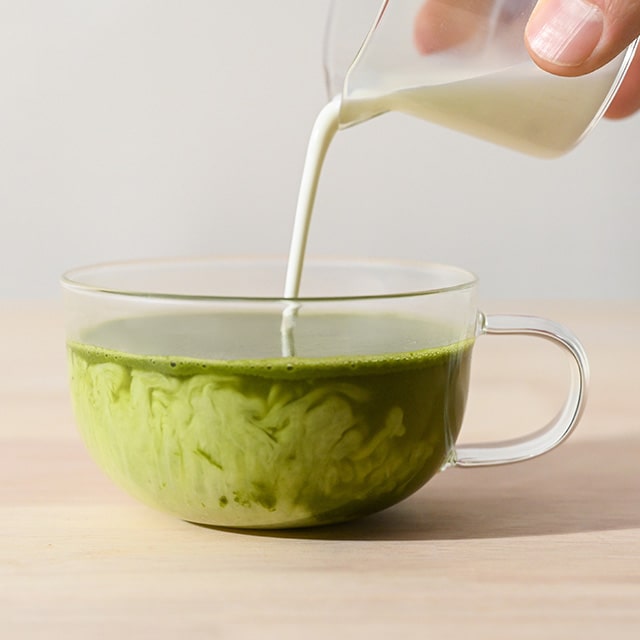 Pouring milk into a cup of green matcha tea.