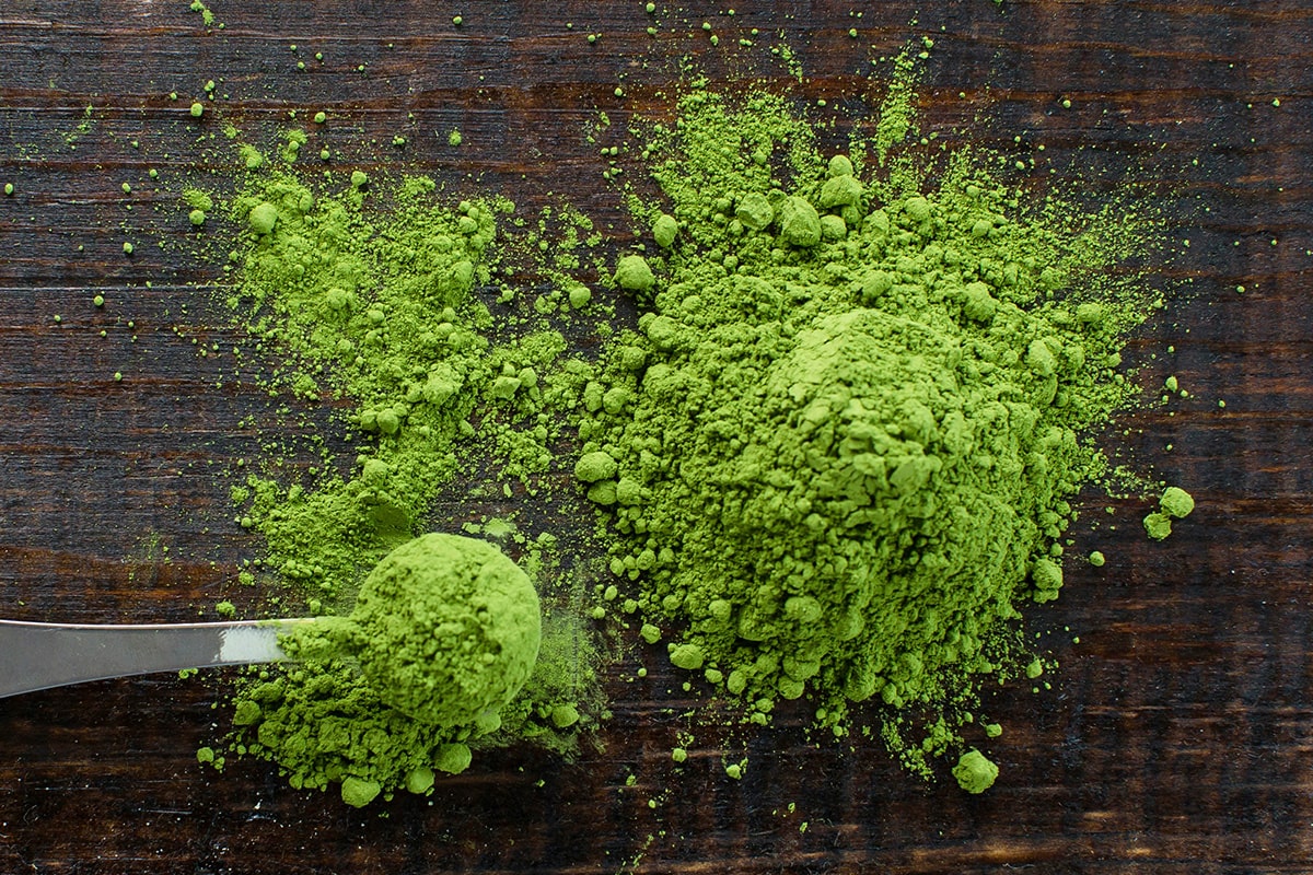 Green powder and a spoon on a wooden surface.