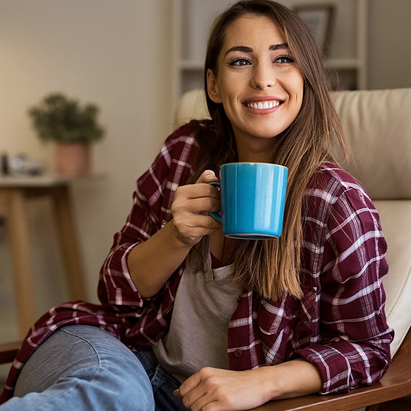 Smiling woman in plaid shirt holding a blue mug, sitting indoors.