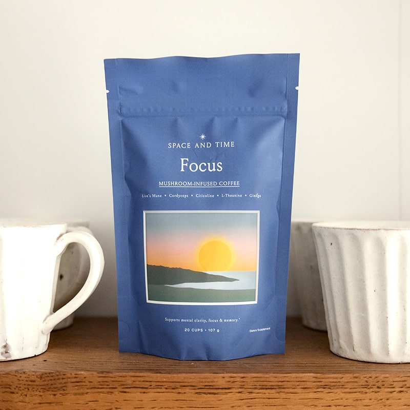 Blue coffee bag labeled 'Focus' with two white mugs on a wooden surface.