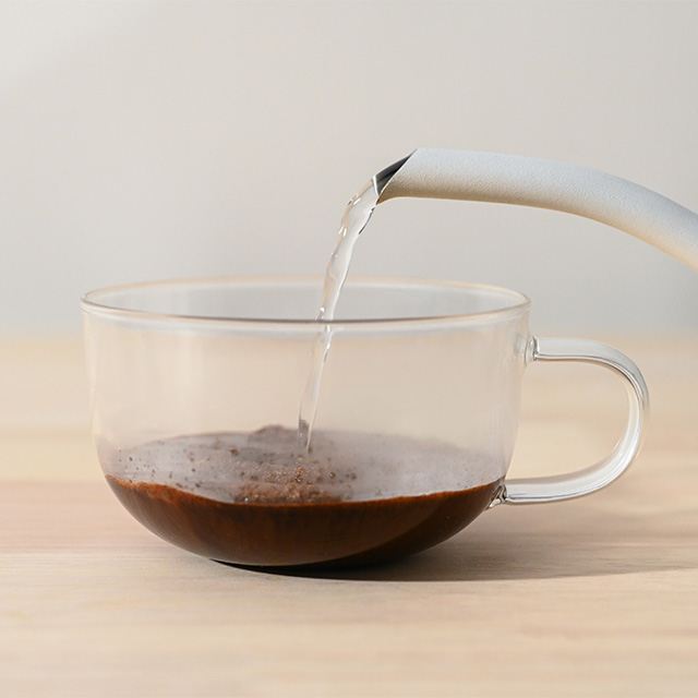 Pouring hot water into a clear cup with coffee grounds.
