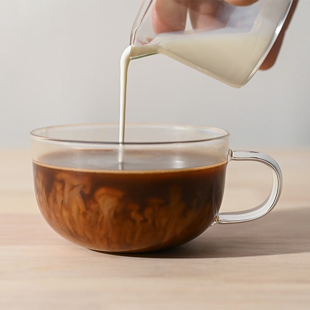 Pouring cream into a glass cup of coffee.