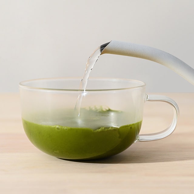 Pouring hot water into a glass cup with green matcha powder.