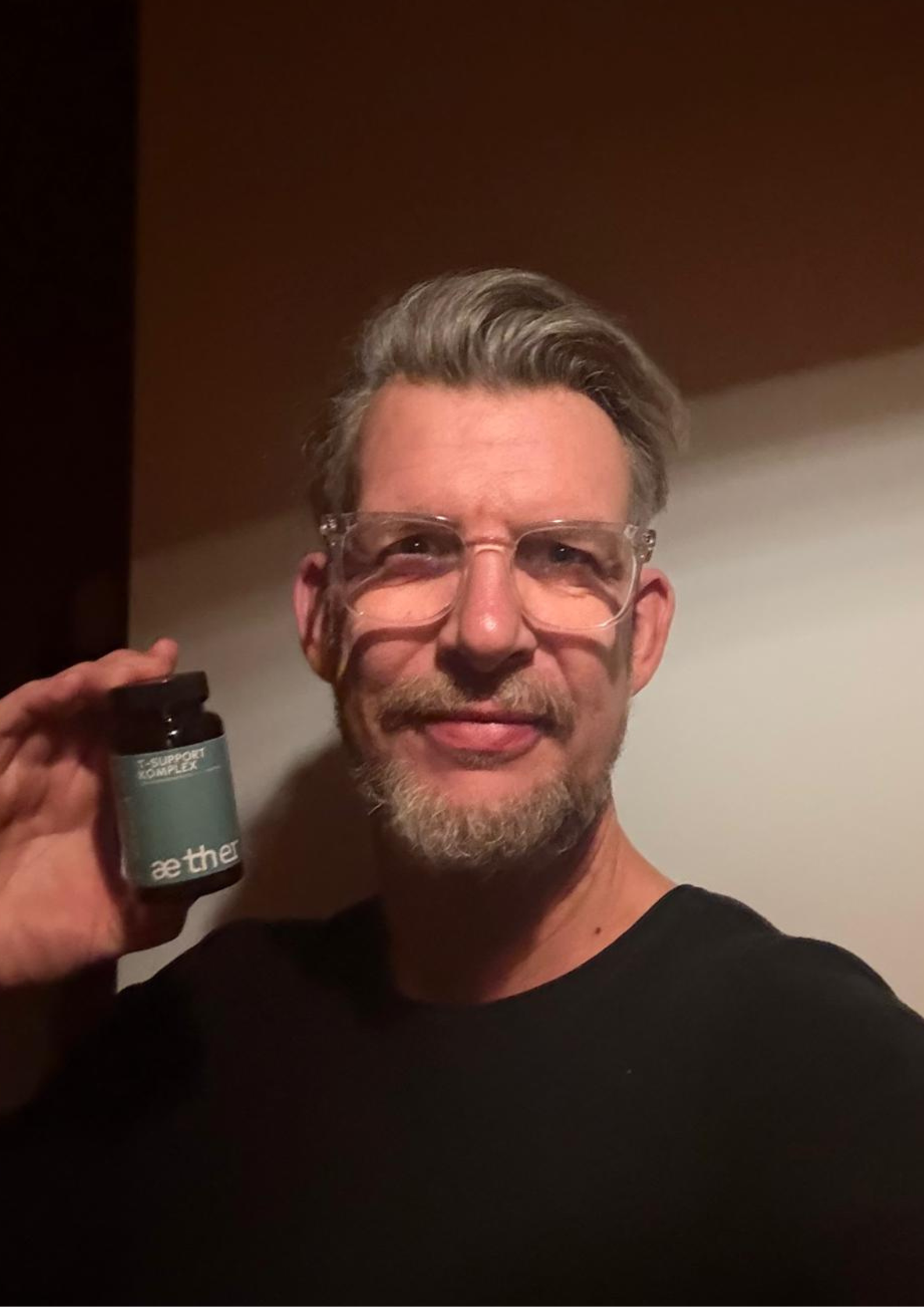 Person holding a bottle labeled 'Aether T-Support Komplex' in a dimly lit room.