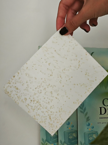 Hand holding a speckled paper over a colorful box.