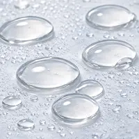 A close-up of clear water droplets of various sizes on a light-colored surface.