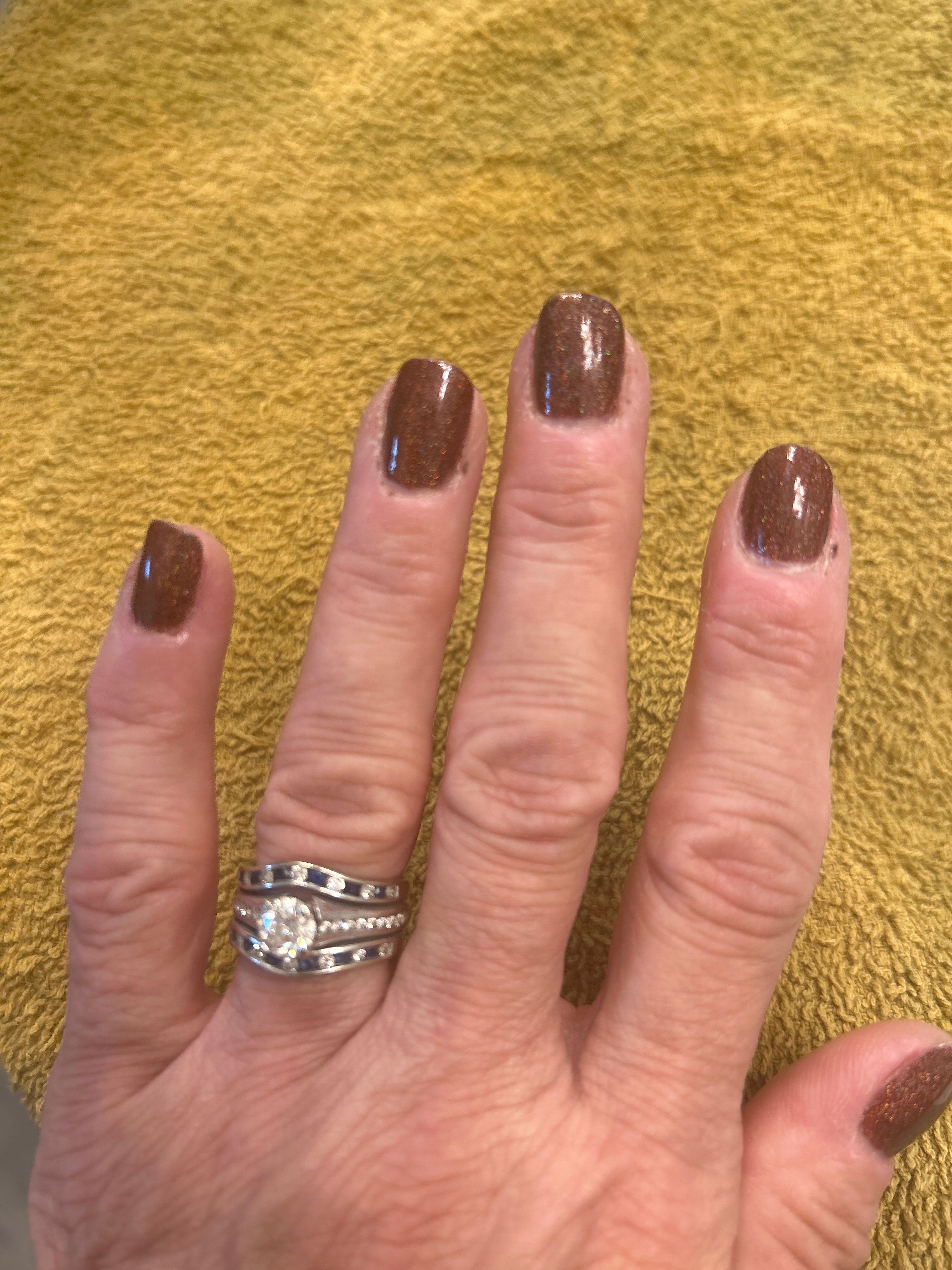 Hand with brown glitter nail polish and a diamond ring on a yellow towel.