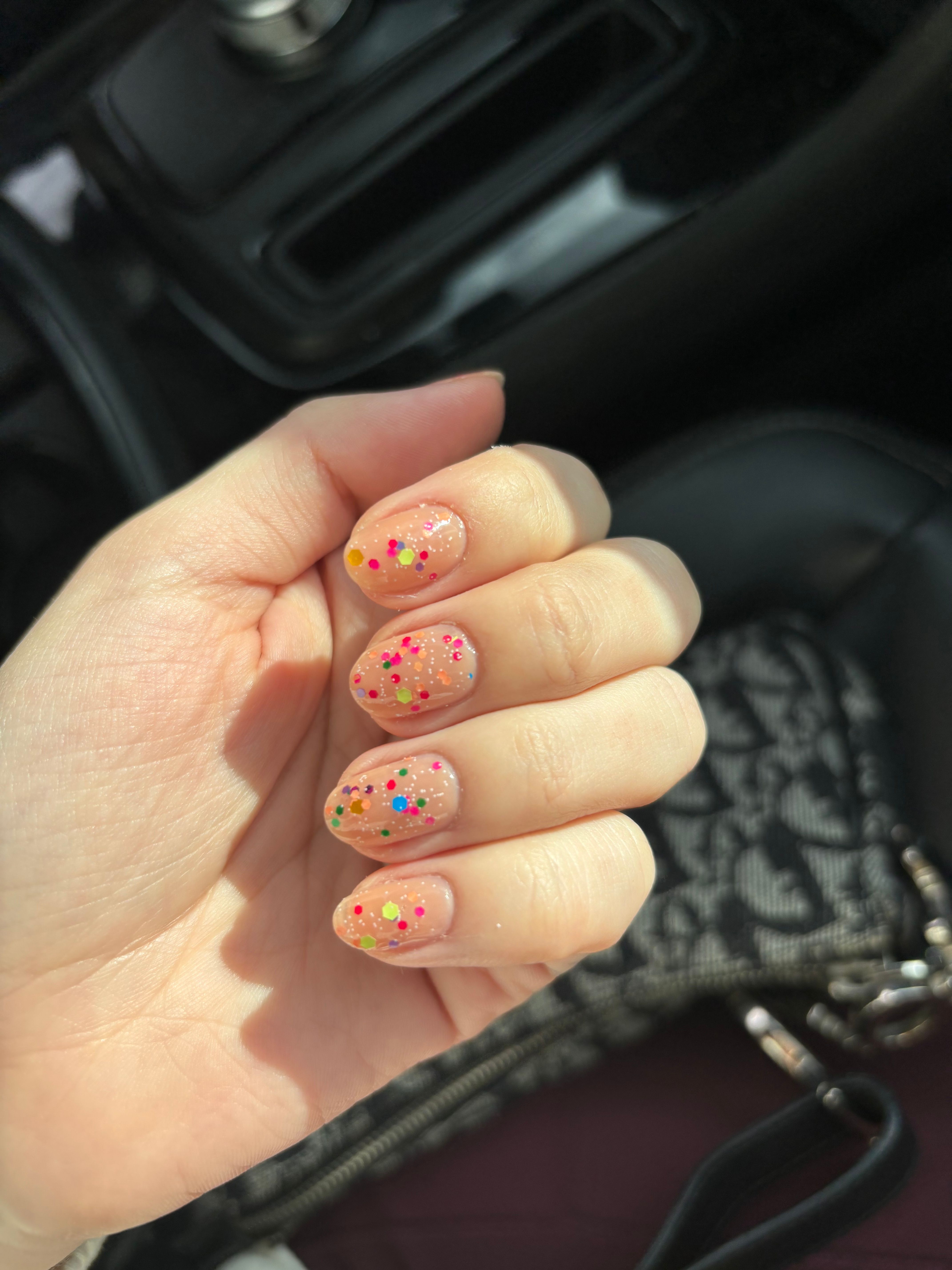 Hand with colorful polka dot nail art in a car interior.