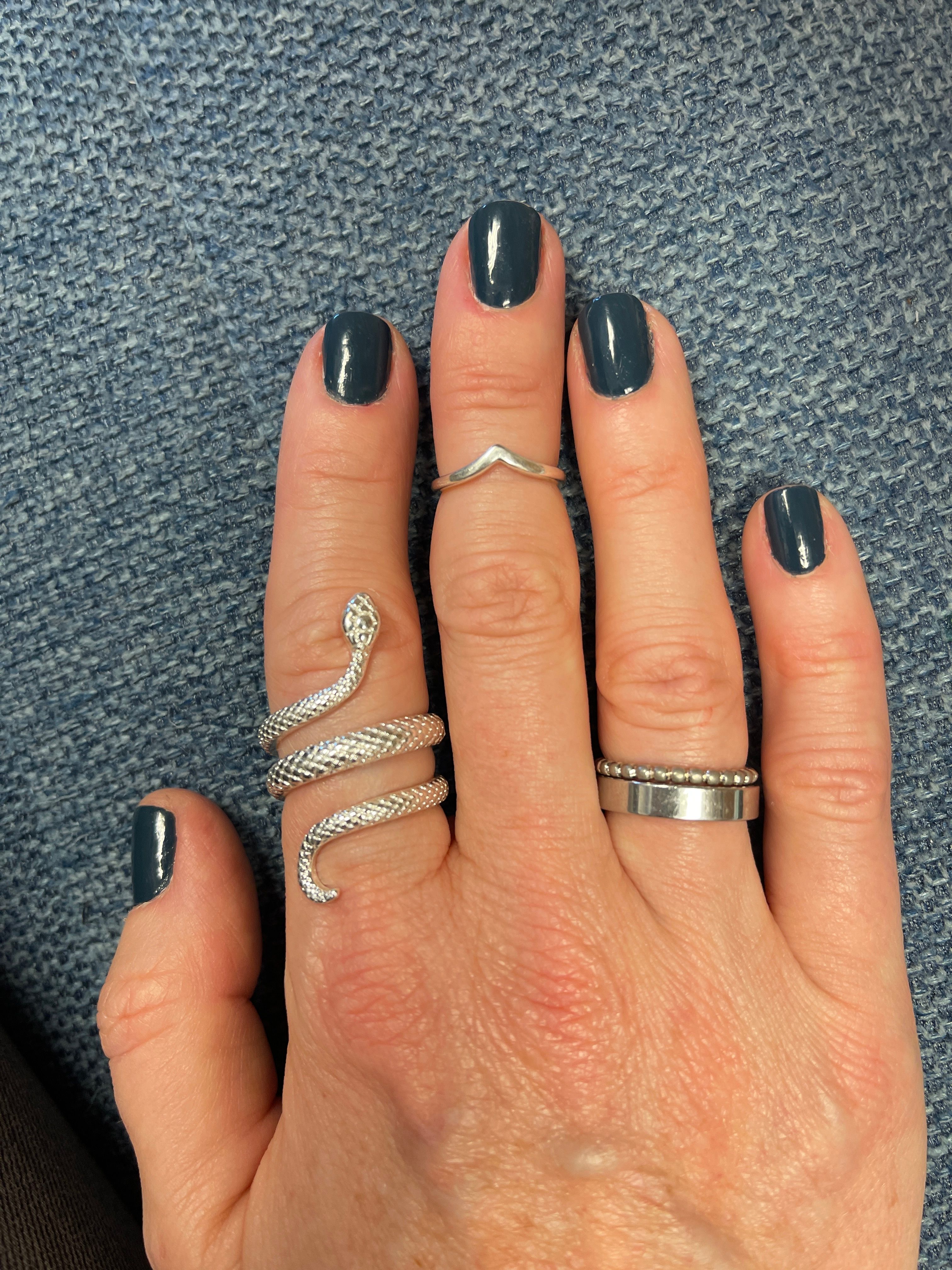 Hand with dark nail polish and multiple silver rings on a textured surface.