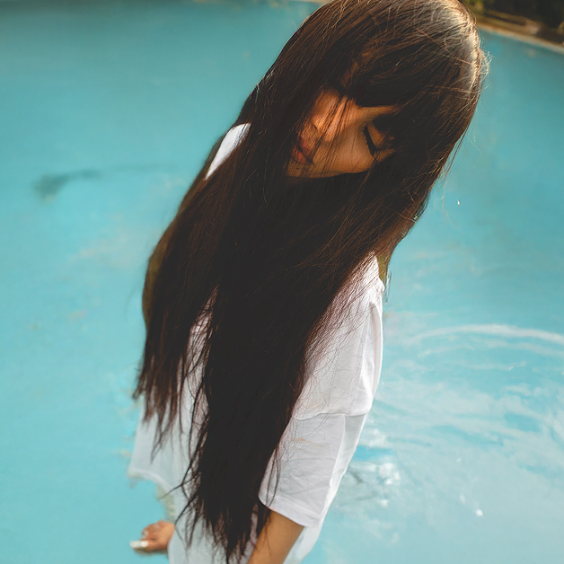 Person with long hair standing in a pool, wearing a white shirt.