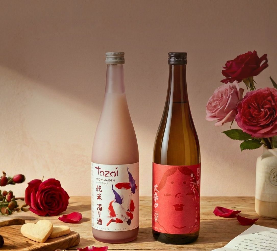Two bottles of sake on a wooden table with roses, heart-shaped cookies, and a letter.