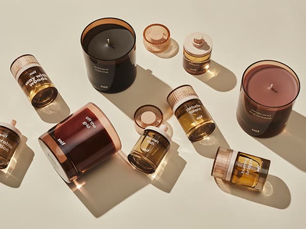 Assorted scented candles and jars on a beige surface.
