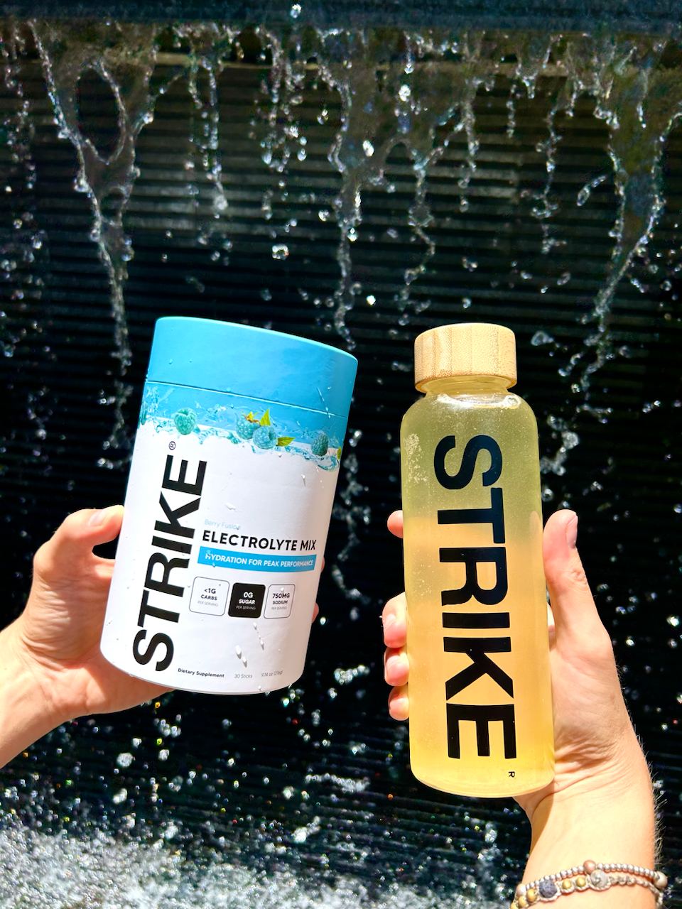 Hands holding a Strike electrolyte mix container and bottle, with water splash background.