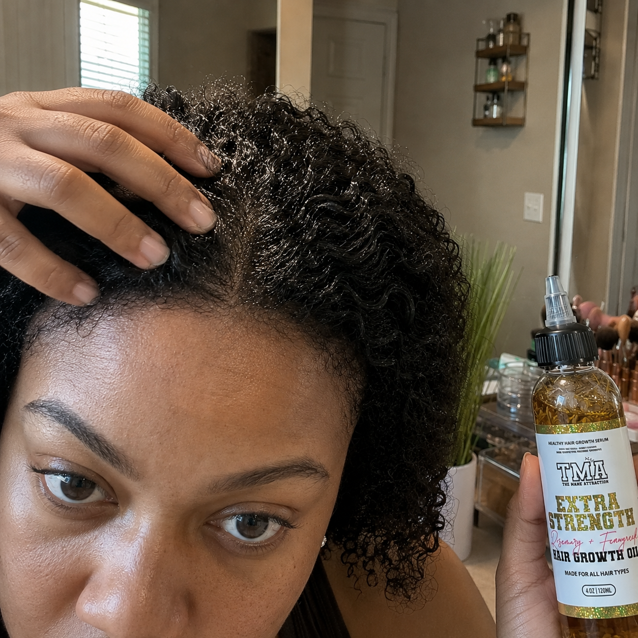 A woman parts her curly hair, showing her scalp while holding a bottle of hair growth oil.