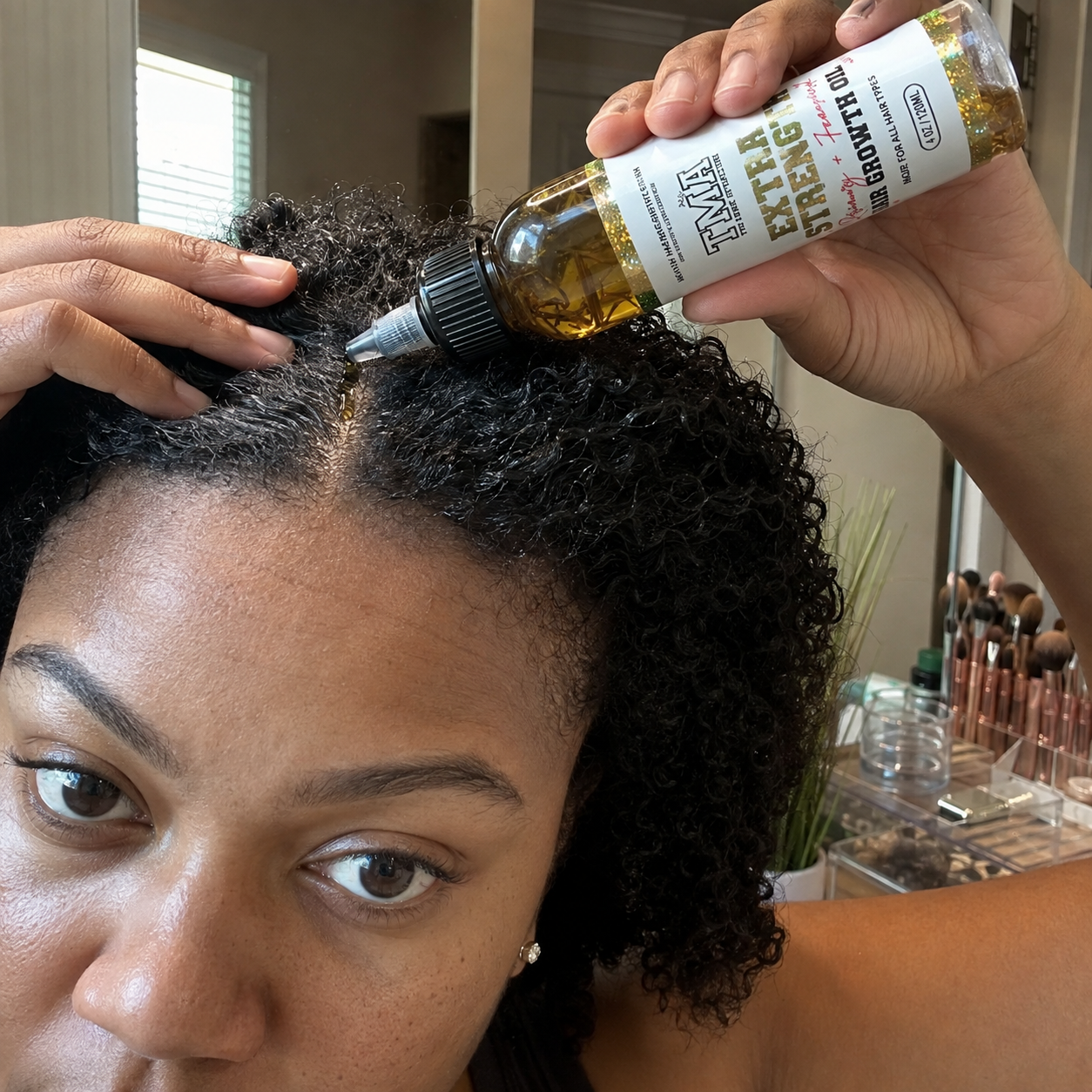 A woman with curly hair parts her hair and applies oil directly to her scalp.